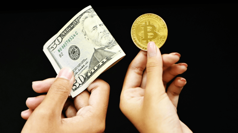 Two hands holding a U.S. dollar bill and a coin with the Bitcoin sign.